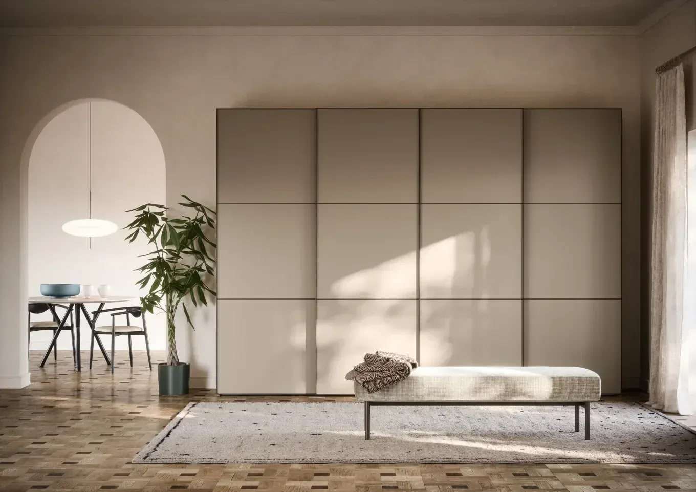 Schuifdeurkast in warm grijs over de hele wand van een lichte kamer, met een bankje ervoor