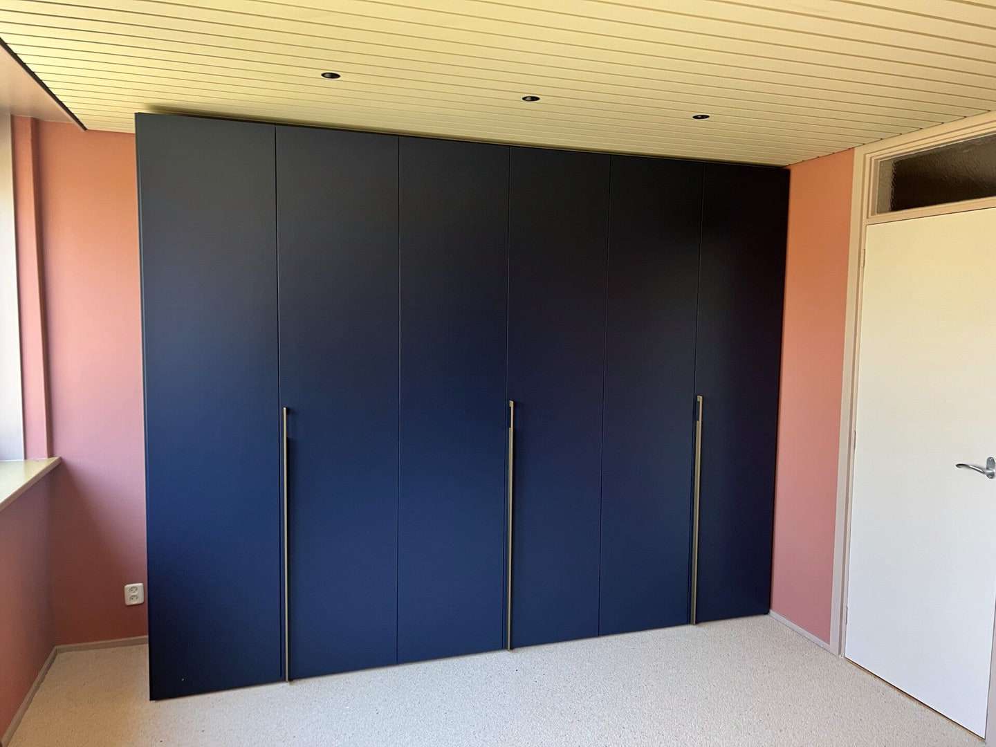 Donkerblauwe kledingkast over de hele wand van een slaapkamer, met de deuren dicht