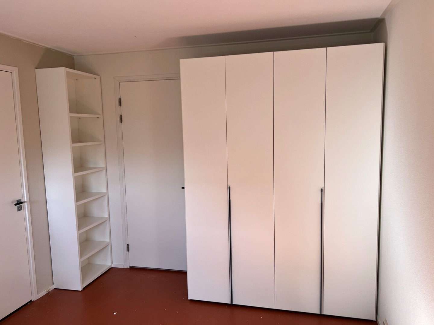 Witte kledingkast met lange zwarte grepen in de hoek van een kamer, met een open kast ernaast