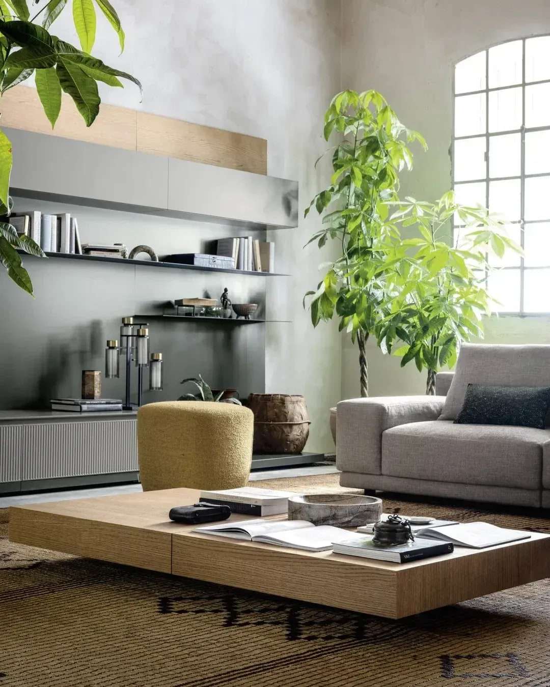 Wandmeubel met open planken en lage kasten in een loft met boogramen, planten en een lage salontafel
