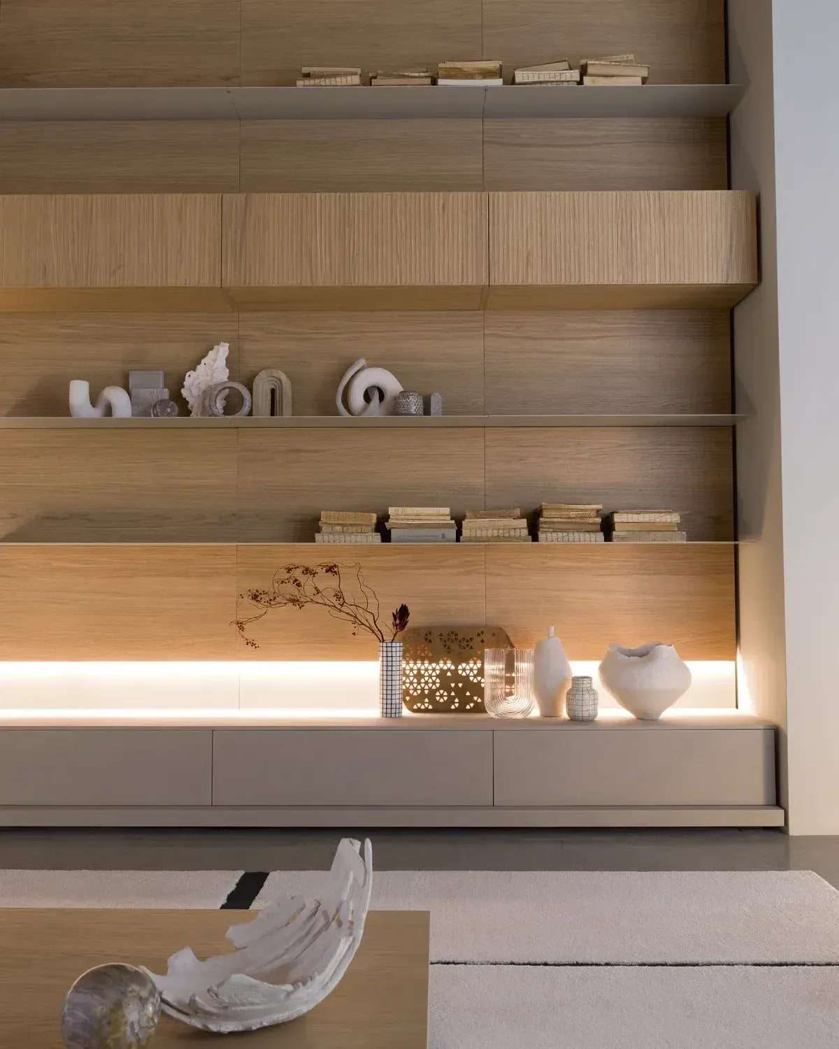 Houten wandkast met open planken, licht onder de planken en een lage witte kast eronder, met vazen en boeken
